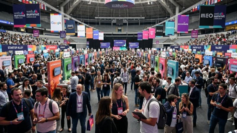 Thousands of tech professionals networking on the exhibition floor at Web Summit Lisbon 2026, with startup booths and sponsor banners filling the MEO Arena venue